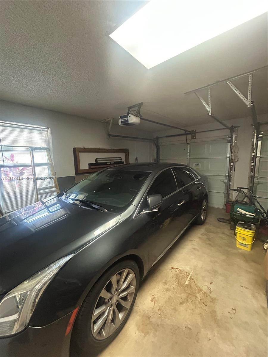 A dark sedan is parked inside a garage with a concrete floor and skylight — LAUDERHILL, FL