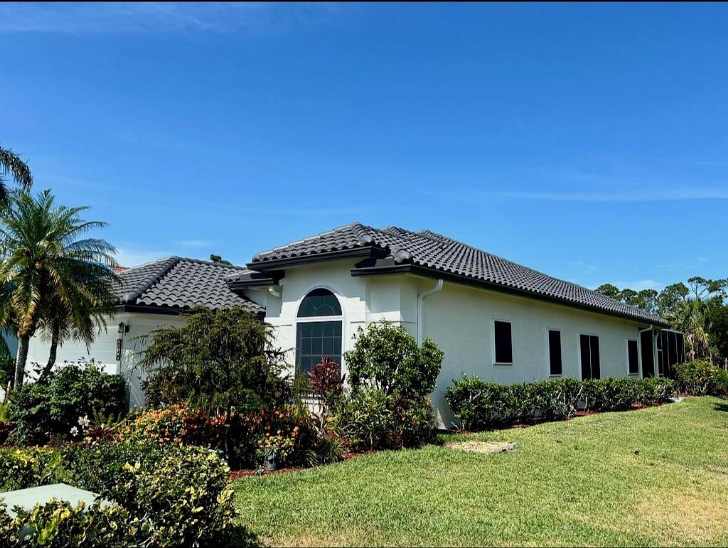 A side view of a white, single-story house with a dark tiled roof and landscaping — 4848 SE Mariner Village Lane, Stuart FL 34997, STUART, FL