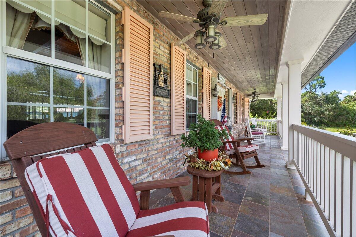 A covered brick porch features rocking chairs, a ceiling fan, and tile flooring — 930 90th Avenue, Vero Beach FL 32966, VERO BEACH, FL