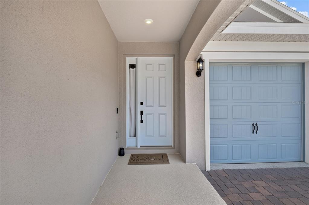 A beige covered entryway features a white front door and a light blue garage door — 2112 KEYSTONE PASS, MINNEOLA, FL