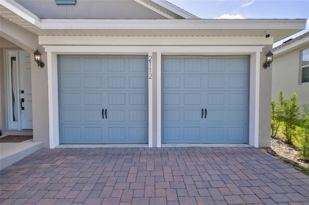 A two-car garage with light blue doors and a brick paver driveway — 2112 KEYSTONE PASS, MINNEOLA, FL