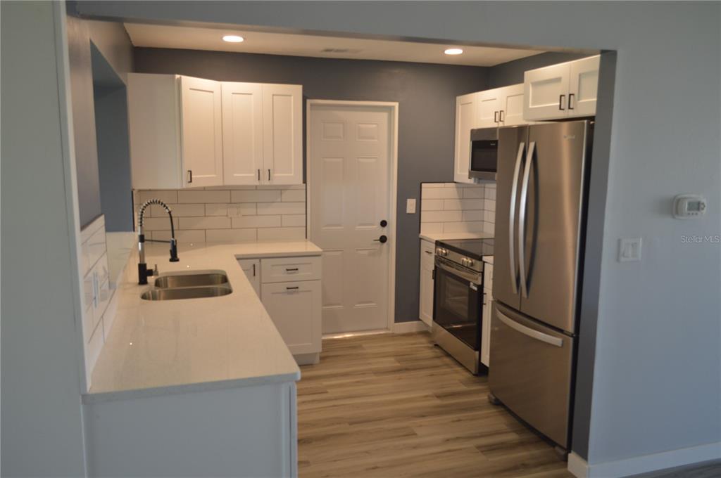 A kitchen features white cabinets, stainless steel appliances, a subway tile backsplash, and light flooring — 3708 97TH AVENUE N, PINELLAS PARK, FL