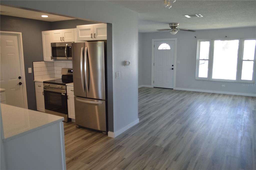 A kitchen with stainless steel appliances and white cabinets opens into a living room area — 3708 97TH AVENUE N, PINELLAS PARK, FL
