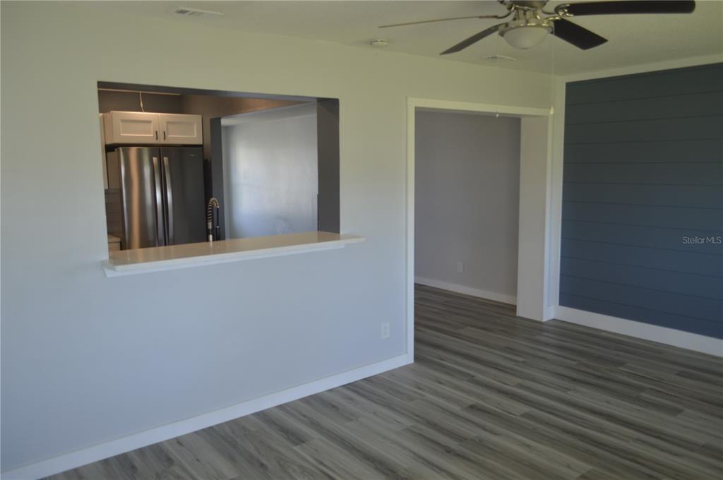 A living room features gray wood-look flooring, a kitchen pass-through window, and a shiplap wall — 3708 97TH AVENUE N, PINELLAS PARK, FL