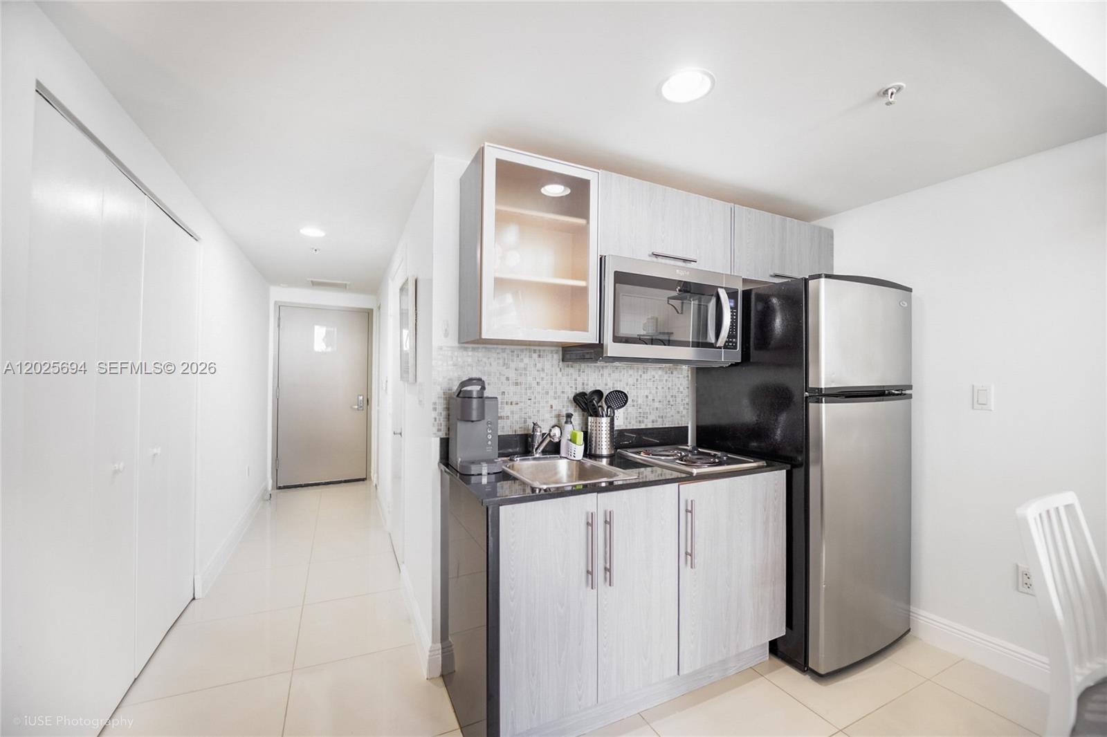 A small kitchen features light wood cabinets, black countertops, stainless steel appliances, and tile flooring — 1750 N Bayshore Dr # 1219, Miami FL 33132, MIAMI, FL