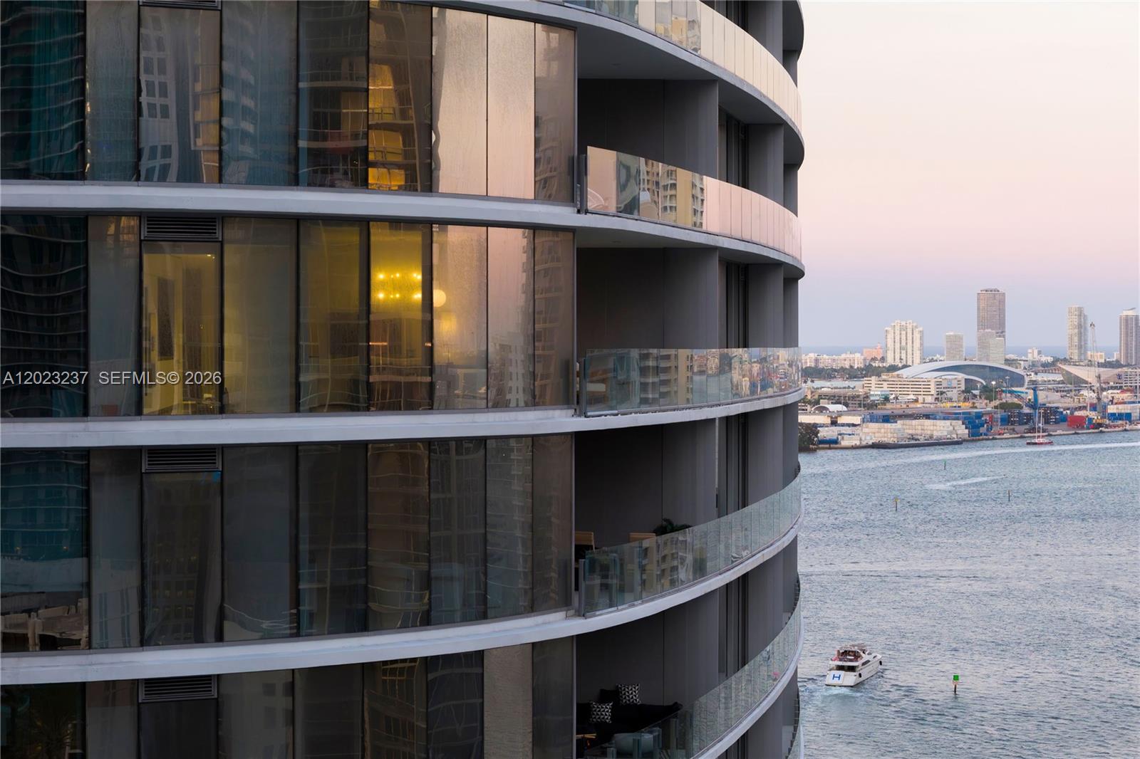 A curved high-rise building exterior features glass balconies overlooking a bay with distant city buildings — 300 S Biscayne Blvd Way # 2107, Miami FL 33131, MIAMI, FL