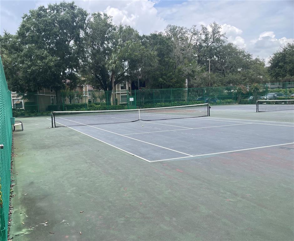 A fenced outdoor tennis court with a net sits in front of apartment buildings — 14308 HANGING MOSS CIRCLE UNIT 101, TAMPA, FL