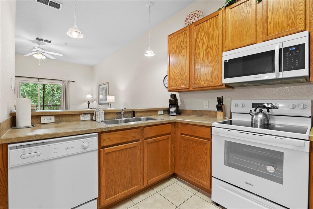 A kitchen with wood cabinets, white appliances, and a double sink under a breakfast bar — 806 GRAN BAHAMA BOULEVARD UNIT 30806, DAVENPORT, FL