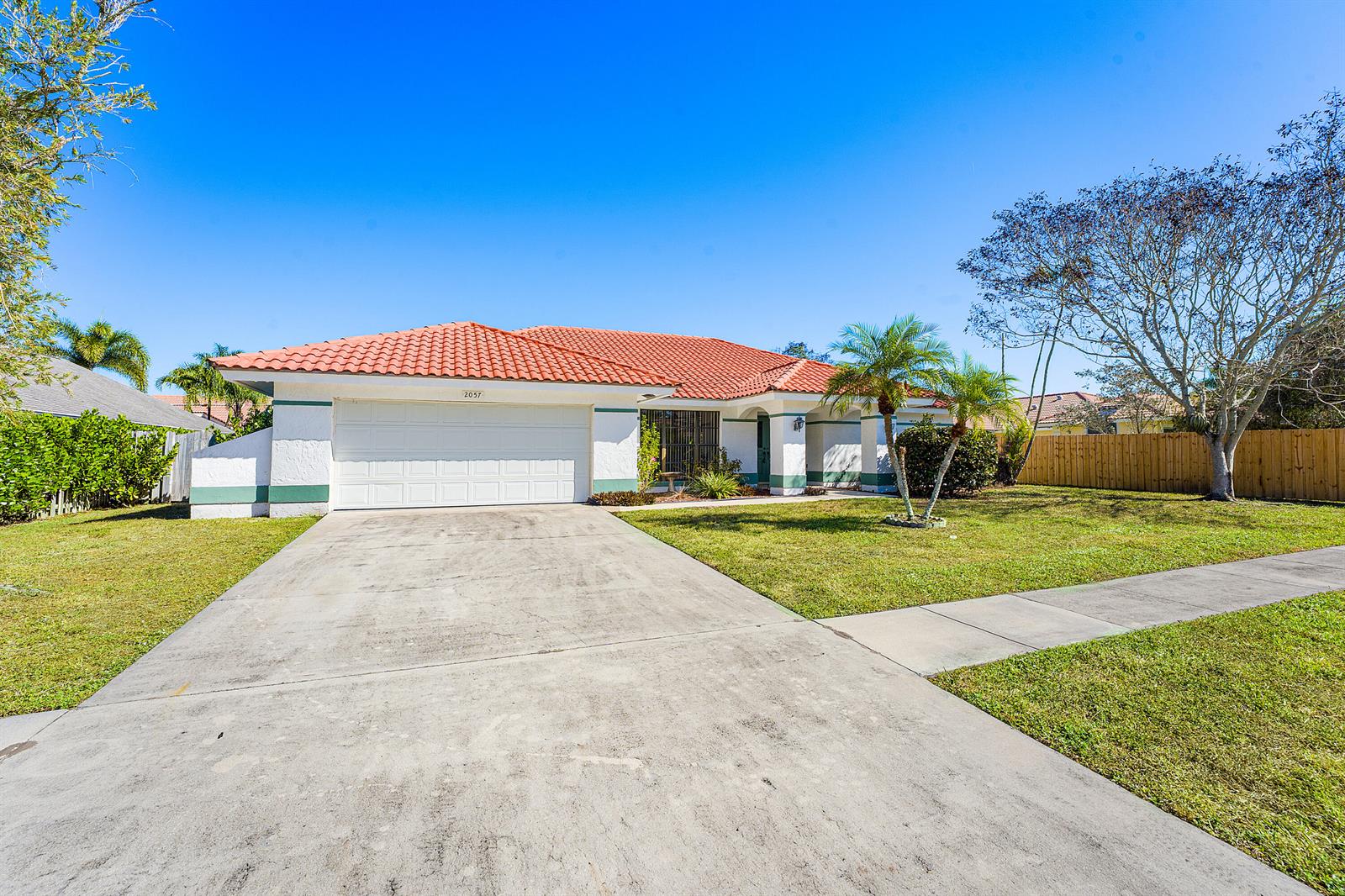 A single-story house with a white stucco exterior, green trim, and a red tile roof — 2057 Amesbury Circle, Wellington FL 33414, WELLINGTON, FL