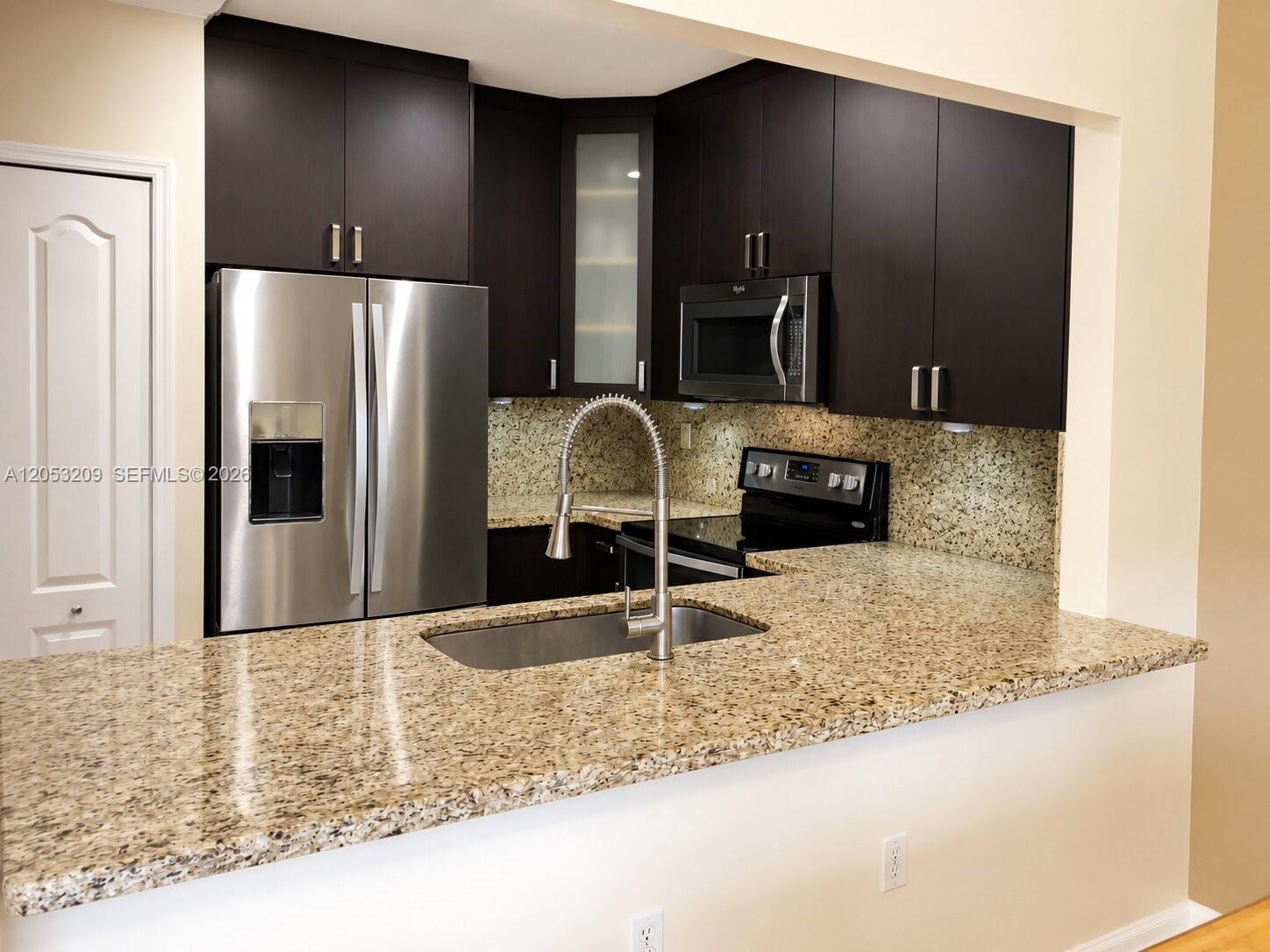 A kitchen features dark wood cabinets, granite countertops, stainless steel appliances, and a sink — 12945 SW 29th St, Miramar FL 33027, MIRAMAR, FL
