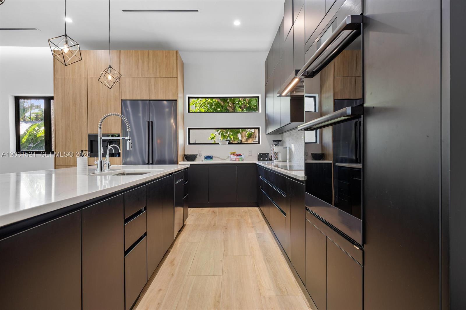 A modern kitchen features black cabinetry, light wood accents, and a large white island — 638 Lakeside Harbor, Boynton Beach FL 33435, BOYNTON BEACH, FL