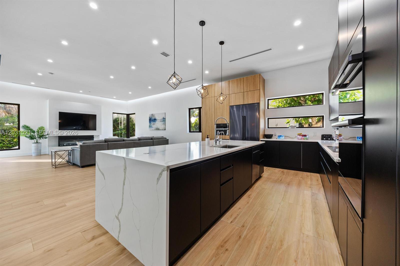 A modern open-concept kitchen features a large marble-topped island, dark cabinetry, and light wood flooring — 638 Lakeside Harbor, Boynton Beach FL 33435, BOYNTON BEACH, FL
