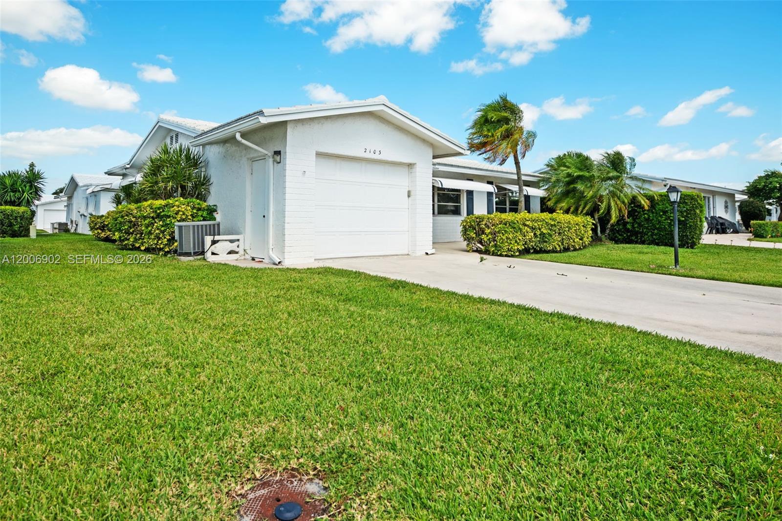 A white single-story house with a garage and a green lawn under a blue sky — 2103 SW 20th Cir, Boynton Beach FL 33426, BOYNTON BEACH, FL