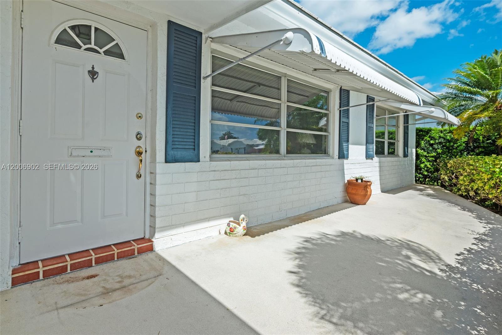 A white brick exterior features a front door, blue shutters, and metal window awnings — 2103 SW 20th Cir, Boynton Beach FL 33426, BOYNTON BEACH, FL