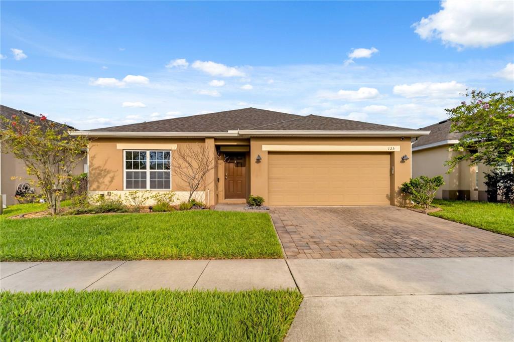 A single-story house with a tan stucco exterior, a two-car garage, and a paved driveway — 125 WILLIAMSON DRIVE, DAVENPORT, FL