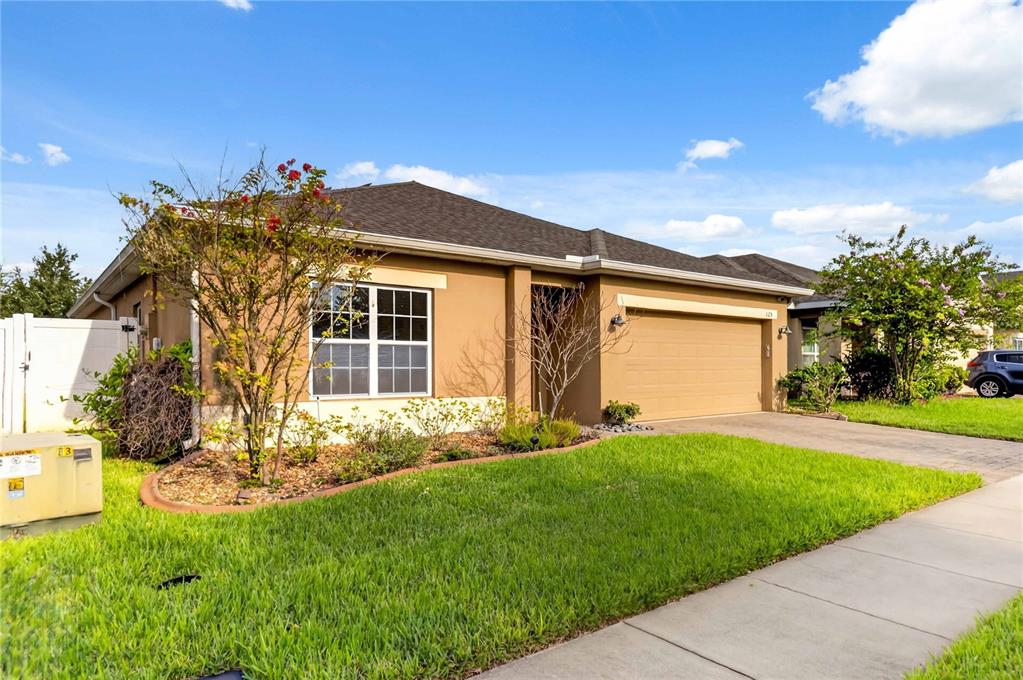A single-story suburban house with a tan stucco exterior, a two-car garage, and a lawn — 125 WILLIAMSON DRIVE, DAVENPORT, FL