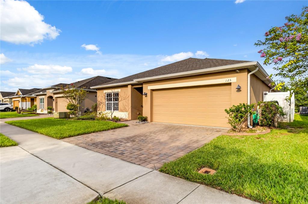 A tan single-story house with a two-car garage and a paved driveway under a blue sky — 125 WILLIAMSON DRIVE, DAVENPORT, FL