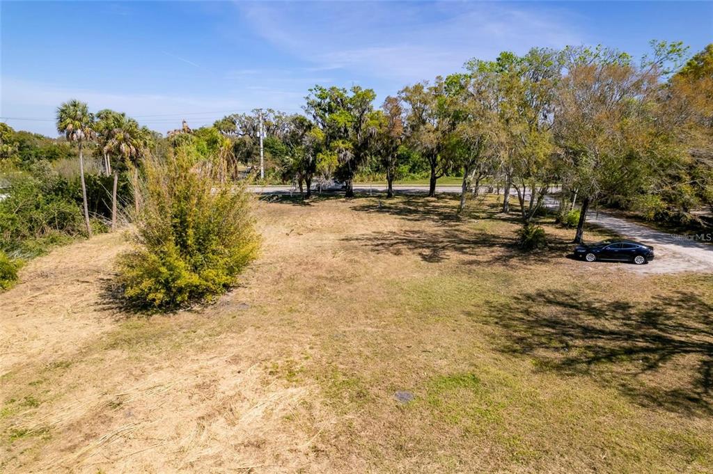 An elevated view shows a large, grassy vacant lot with scattered trees and a parked car — 2619 16TH AVENUE DRIVE E, BRADENTON, FL