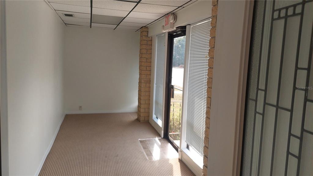 An empty office space features beige carpet, white walls, a drop ceiling, and brick pillars — 1115 NW 13TH STREET, GAINESVILLE, FL