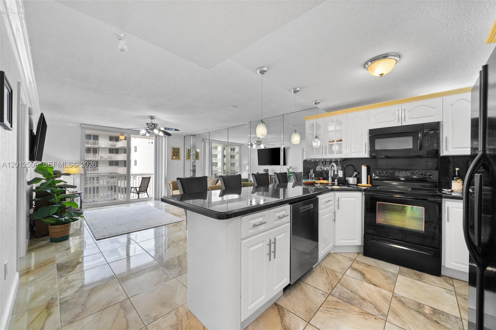 A kitchen with white cabinets and black appliances features a breakfast bar and tiled floors — 401 Ocean Dr # 509, Miami Beach FL 33139, MIAMI BEACH, FL