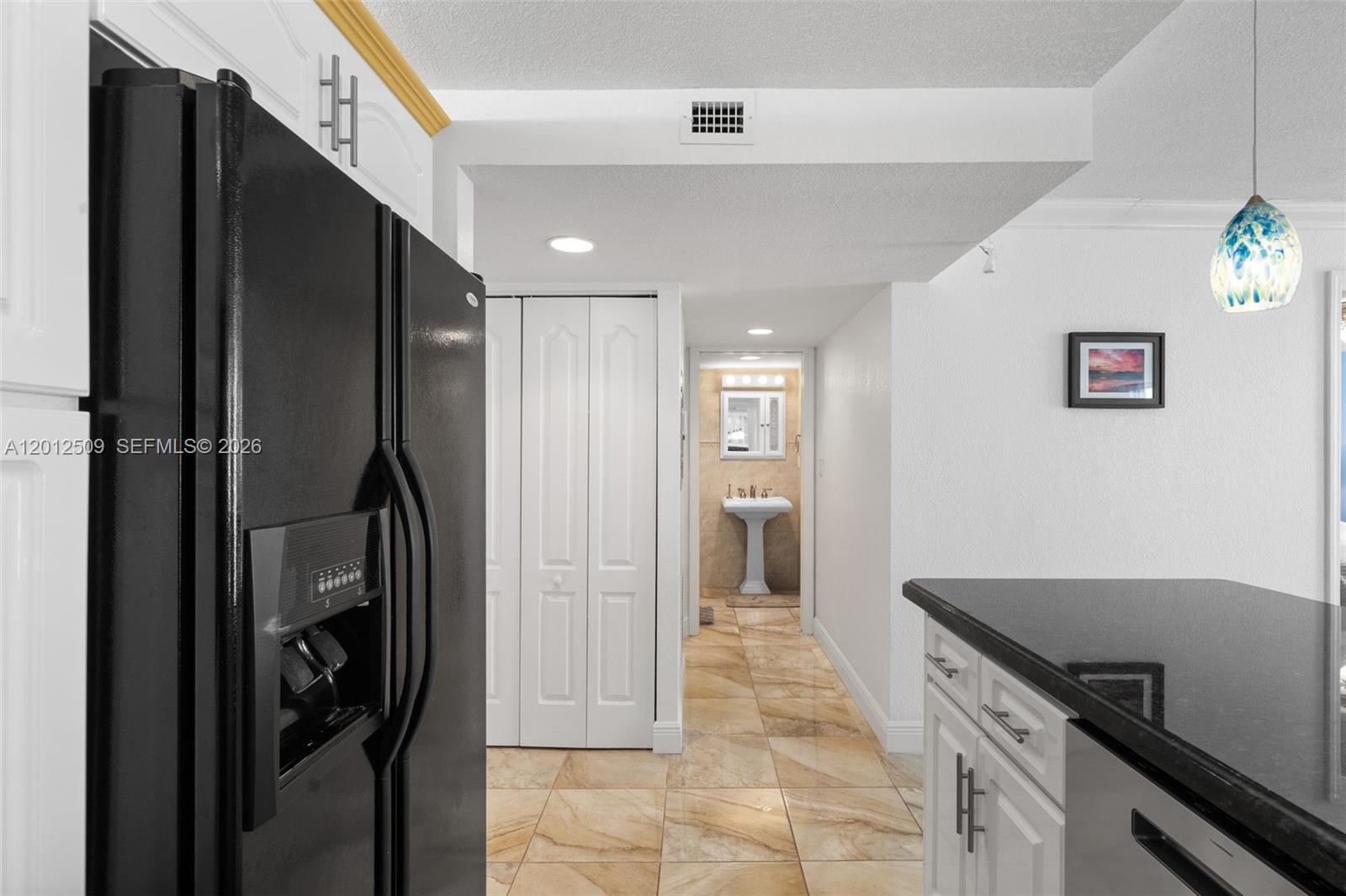 A kitchen with a black refrigerator and island leads to a hallway with a bathroom — 401 Ocean Dr # 509, Miami Beach FL 33139, MIAMI BEACH, FL