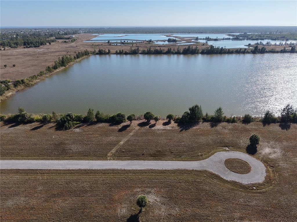 An aerial view shows a vacant lot with a cul-de-sac road bordering a lake — 8 CHINABERRY WAY, PLACIDA, FL