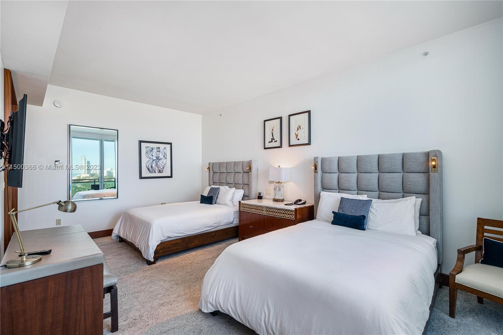 A bedroom features two beds with gray tufted headboards, a nightstand, and a desk — 10295 Collins Ave # 1216, Bal Harbour FL 33154, BAL HARBOUR, FL