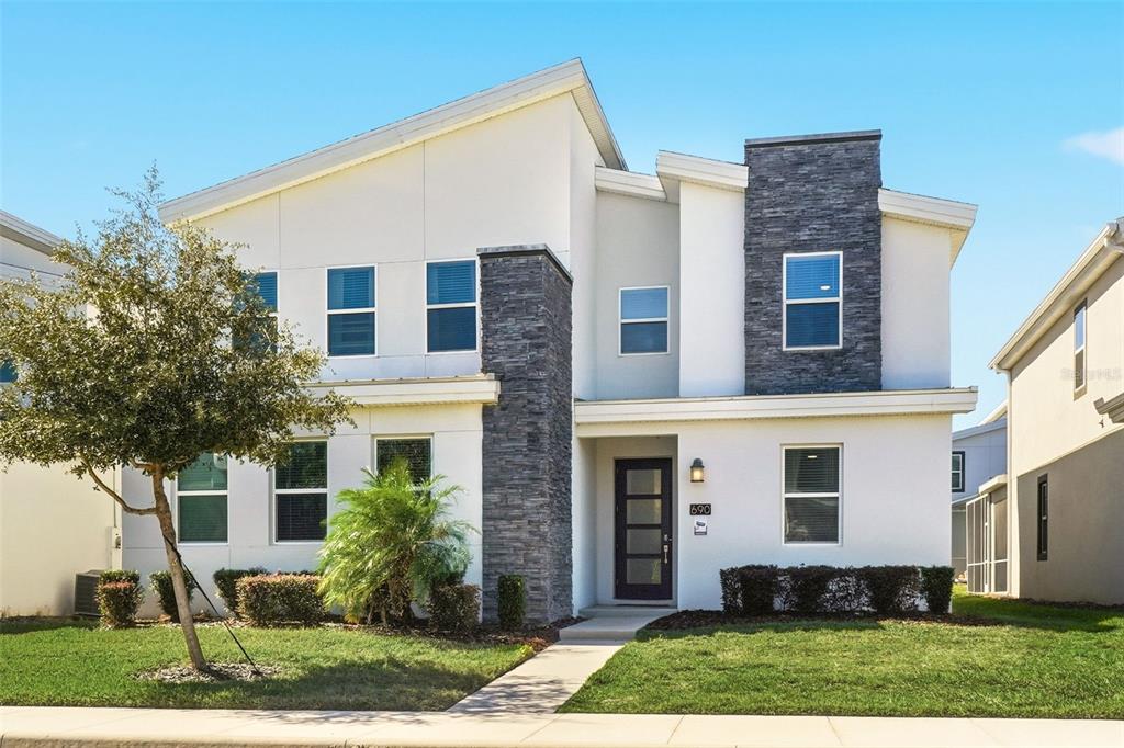 A two-story house with white stucco walls, dark stone accents, and a modern front door — 690 DROP SHOT DRIVE, DAVENPORT, FL
