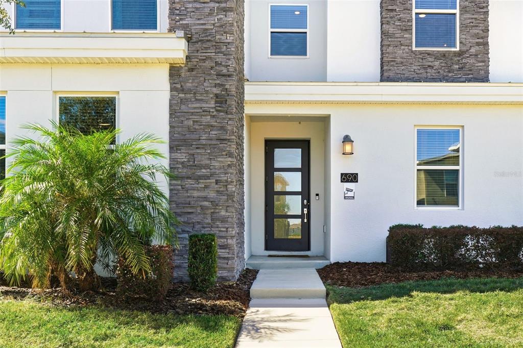 The exterior of a modern home features a stone-accented facade, a dark door, and landscaping — 690 DROP SHOT DRIVE, DAVENPORT, FL