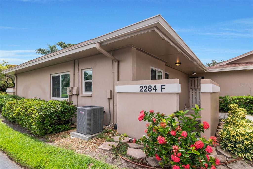 A tan exterior of a single-story building with a small garden and air conditioning unit — 2284 OAK NECK ROAD UNIT F, CLEARWATER, FL
