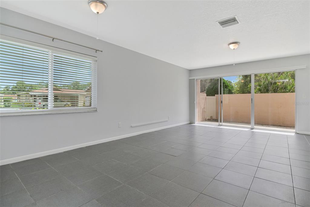 An empty room features gray tile flooring, light gray walls, and a sliding glass door — 2284 OAK NECK ROAD UNIT F, CLEARWATER, FL