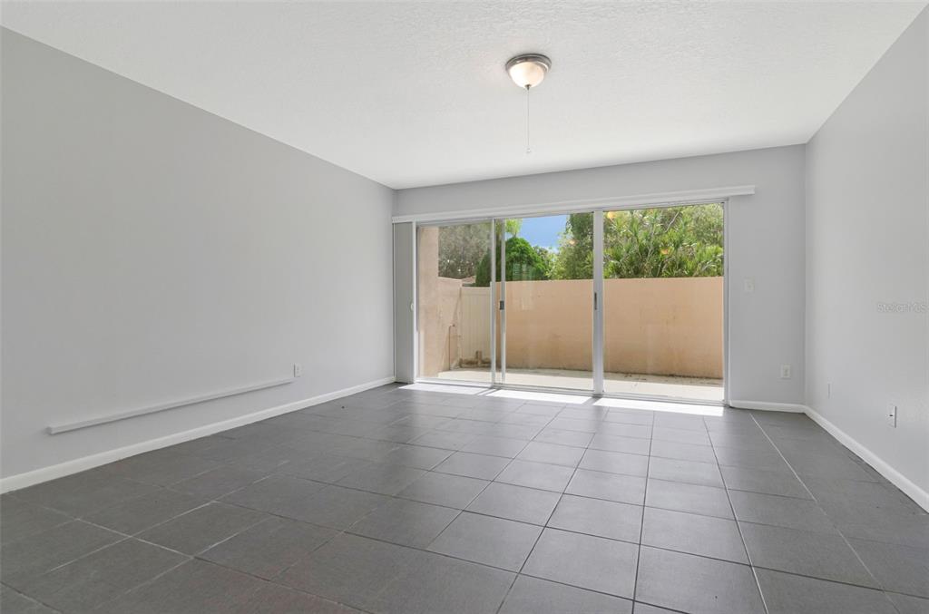 A room with gray tile flooring, light gray walls, and a sliding glass door — 2284 OAK NECK ROAD UNIT F, CLEARWATER, FL