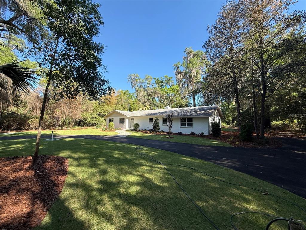 A white, single-story house sits on a grassy lot with a curved asphalt driveway — 4890 NW 20TH PLACE, GAINESVILLE, FL