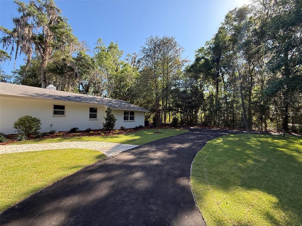 A white brick house with a paved driveway and lawn surrounded by mature trees — 4890 NW 20TH PLACE, GAINESVILLE, FL