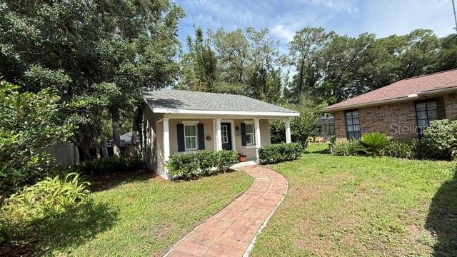 A small, light-colored house with a front porch and a brick walkway sits in a yard — 1990 LARCHMONT DRIVE, DELAND, FL
