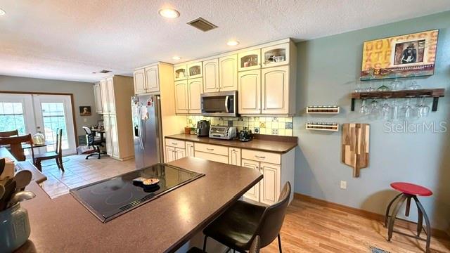 A kitchen features cream-colored cabinets, a central island with a cooktop, and a wine rack — 1990 LARCHMONT DRIVE, DELAND, FL