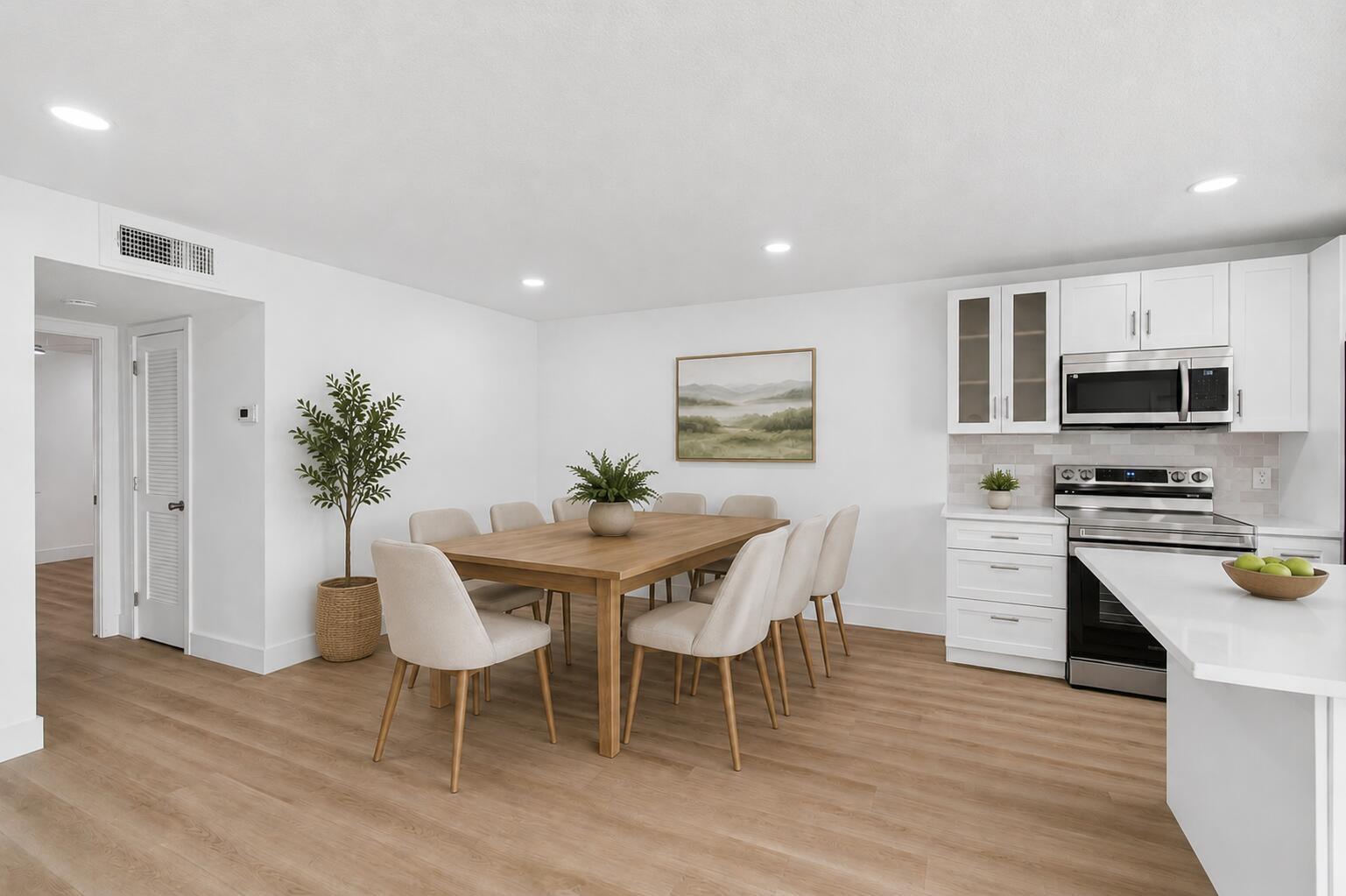 A dining area with a wooden table and chairs sits next to a white kitchen — 1007 South Drive, Delray Beach FL 33445, DELRAY BEACH, FL