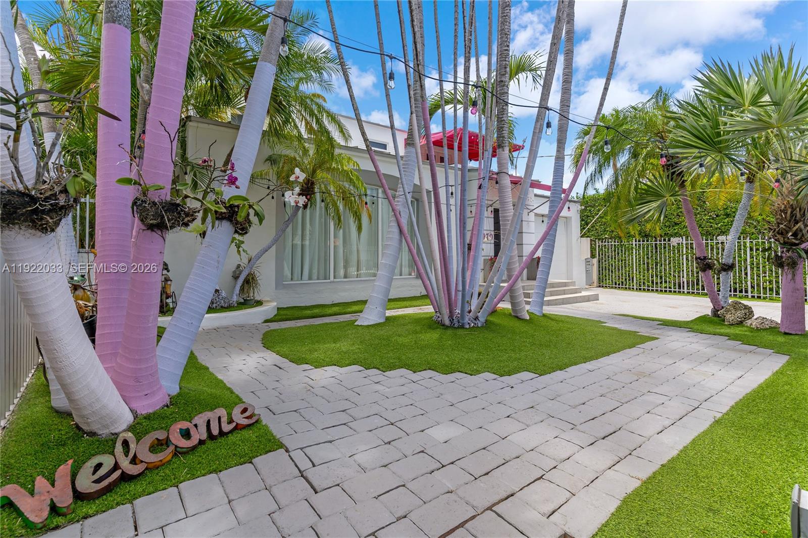 A front yard features a paved walkway, artificial turf, and palm trees painted with pink accents — 3470 Sheridan Ave, Miami Beach FL 33140, MIAMI BEACH, FL