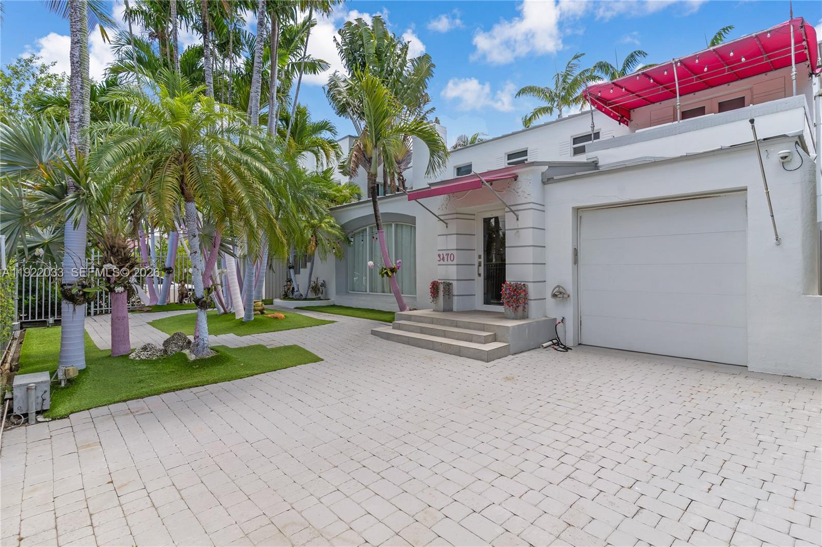 A white two-story house features a paved driveway, palm trees, and a pink awning — 3470 Sheridan Ave, Miami Beach FL 33140, MIAMI BEACH, FL