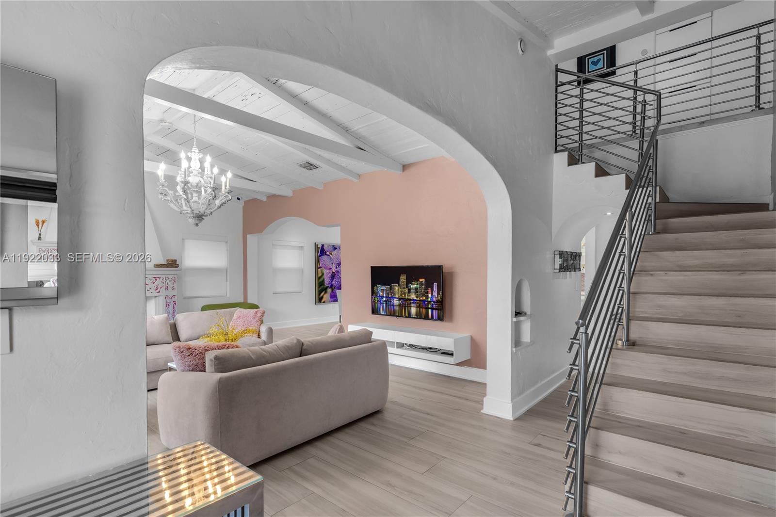 A living room features a pink accent wall, arched entryway, and a staircase with railing — 3470 Sheridan Ave, Miami Beach FL 33140, MIAMI BEACH, FL