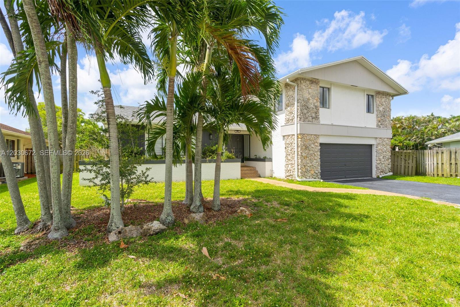 A two-story house with a stone facade, a gray garage door, and palm trees outside — 9340 NW 32nd St, Sunrise FL 33351, SUNRISE, FL