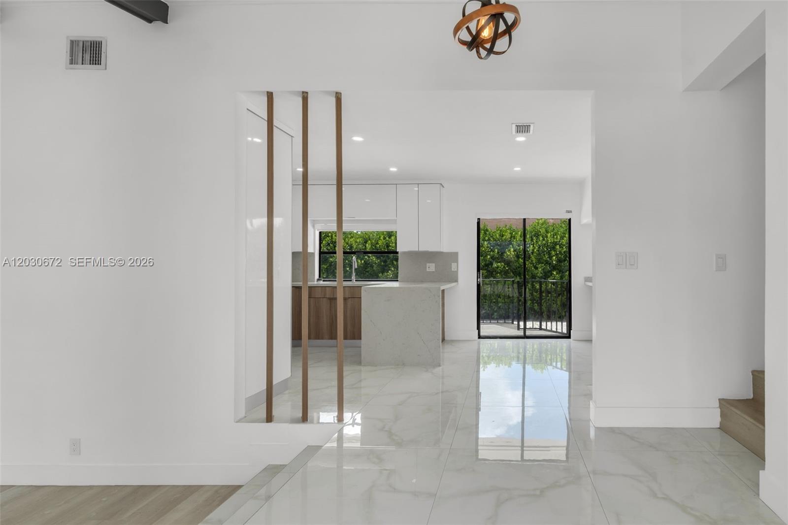 A modern kitchen with white cabinets and wood accents is viewed through a slatted partition — 9340 NW 32nd St, Sunrise FL 33351, SUNRISE, FL