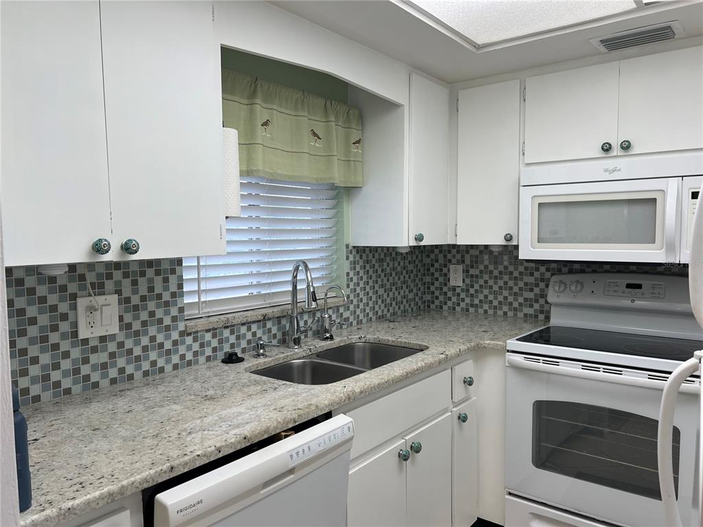 A kitchen features white cabinets, granite countertops, a mosaic tile backsplash, and white appliances — 3751 S SCHOOL AVENUE UNIT 29, SARASOTA, FL