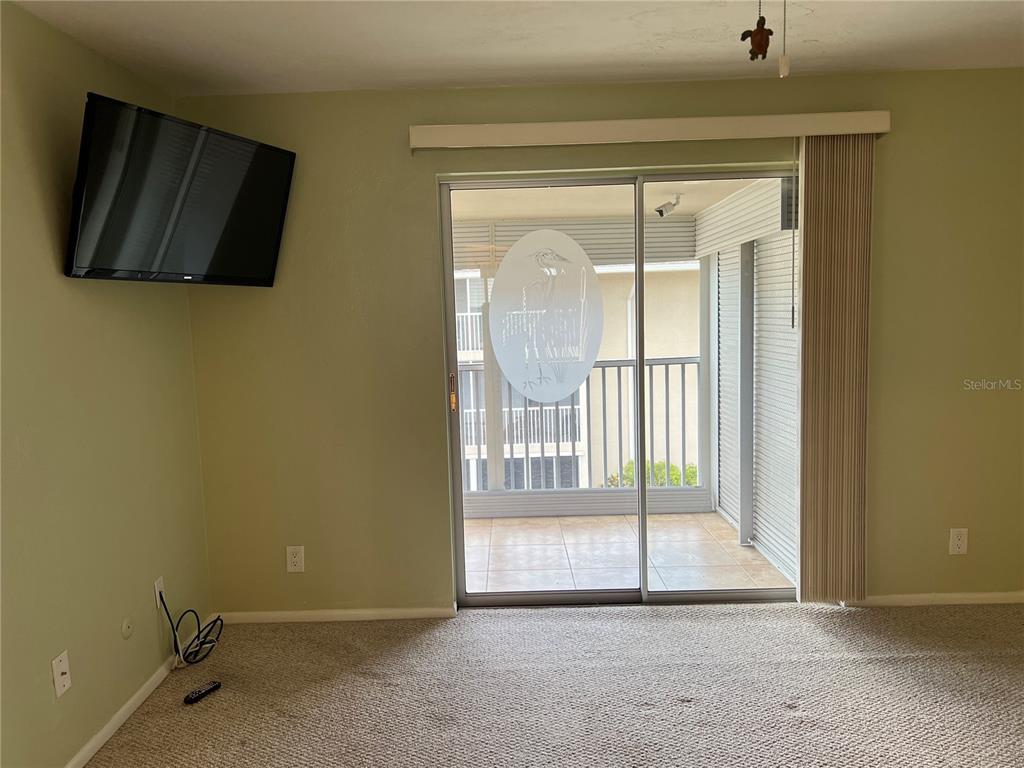 A carpeted living room features a wall-mounted television and a sliding glass door to a balcony — 3751 S SCHOOL AVENUE UNIT 29, SARASOTA, FL