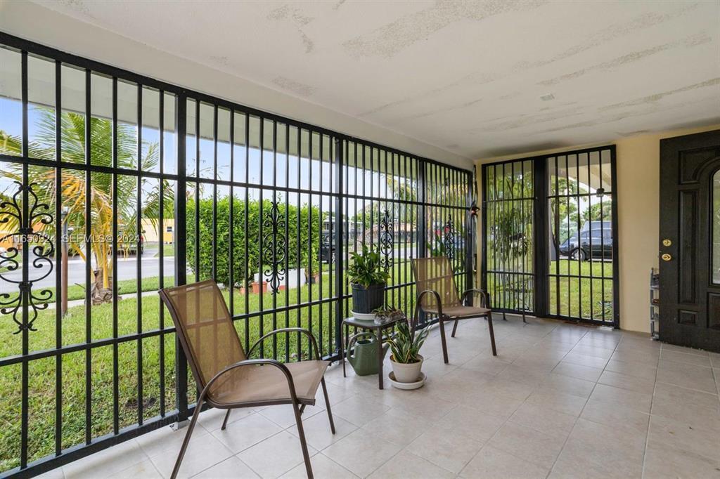 A covered porch features tiled flooring, two chairs, potted plants, and black metal security bars — 18930 NW 14th Avenue, Miami FL 33169, MIAMI, FL