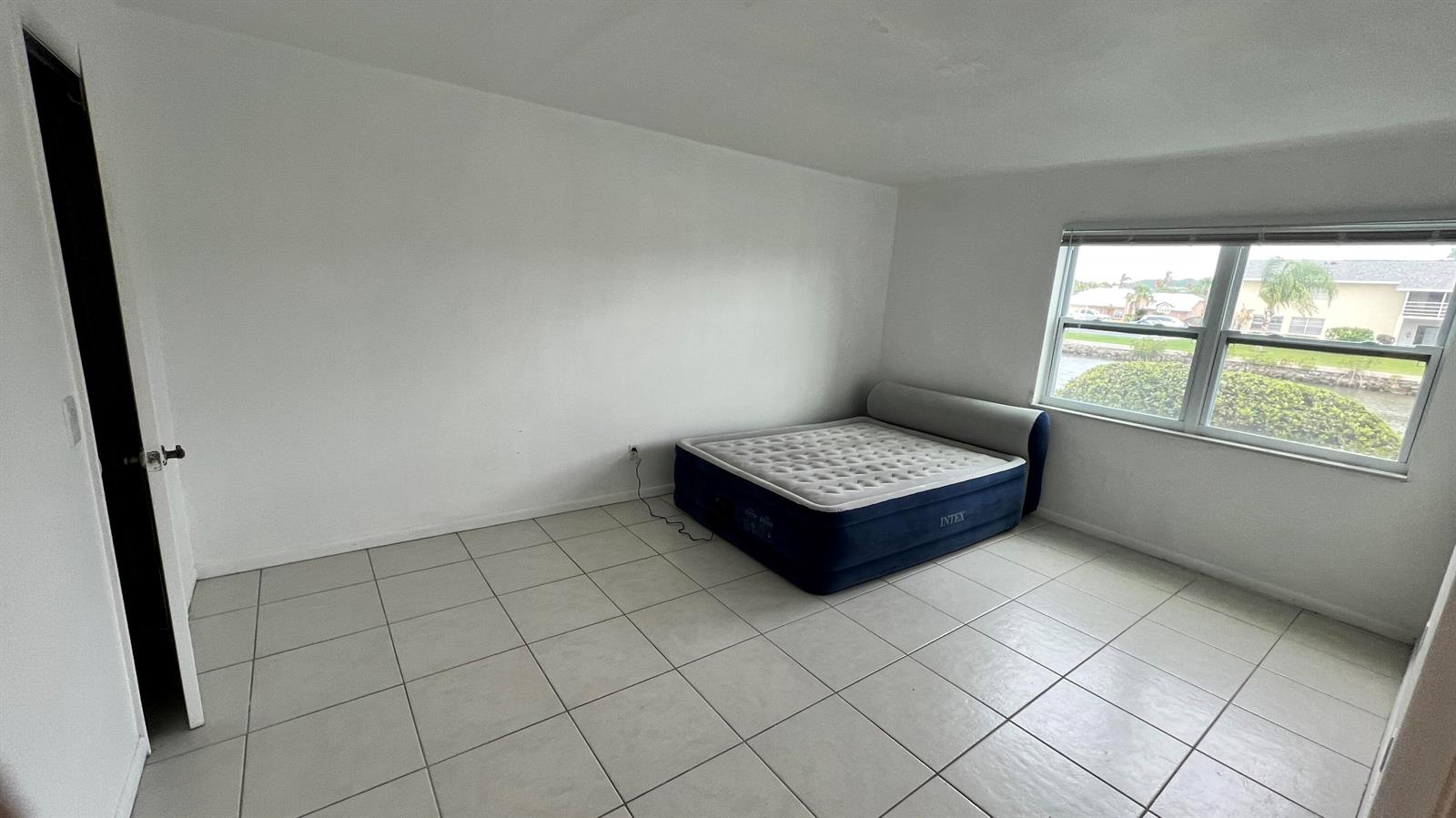 A bedroom with white walls, tiled flooring, and an inflatable mattress near a window — 1860 Robalo Drive # 104, Vero Beach FL 32960, VERO BEACH, FL