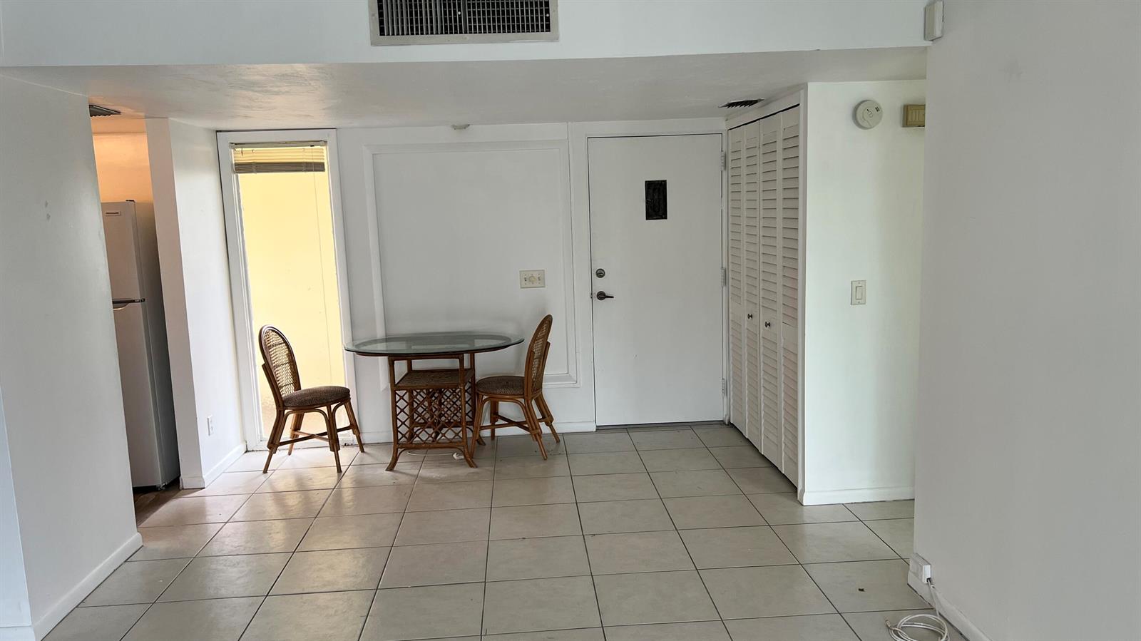 A dining area with a glass table, two chairs, tile flooring, and a white door — 1860 Robalo Drive # 104, Vero Beach FL 32960, VERO BEACH, FL