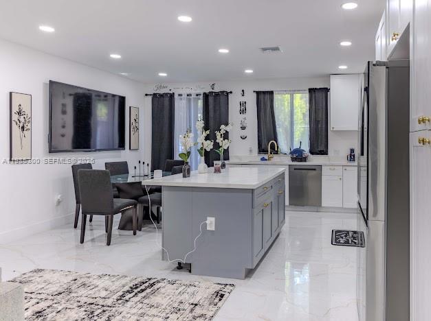 A modern kitchen features a gray island, white cabinetry, stainless steel appliances, and tile flooring — 666 NE 164th Ter, Miami FL 33162, MIAMI, FL