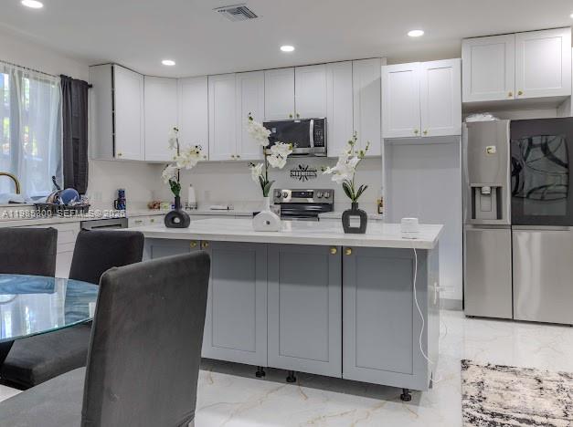 A modern kitchen features white upper cabinets, a gray island, and stainless steel appliances — 666 NE 164th Ter, Miami FL 33162, MIAMI, FL