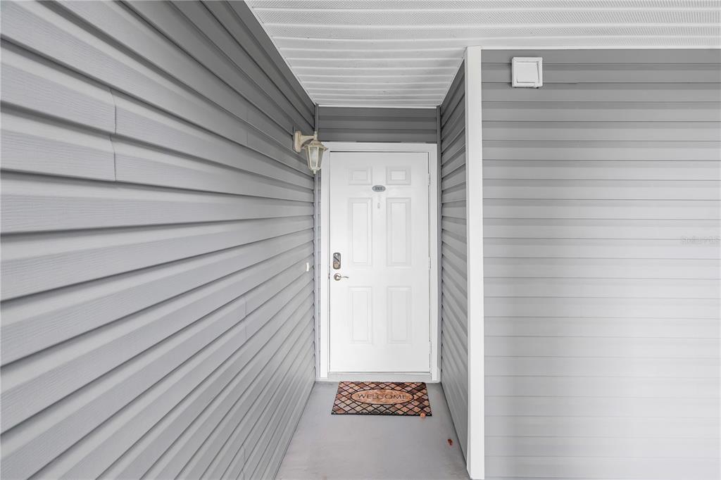 A white front door with a welcome mat is set within a gray-sided entryway — 6924 STONES THROW CIRCLE N UNIT 8103, ST PETERSBURG, FL